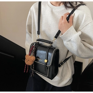 Detailed view of a retro black leather dual-use bag featuring golden hardware and a cute bear charm