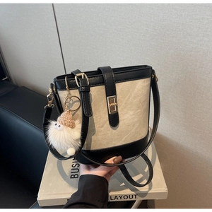 Close-up of beige canvas and black leather bucket bag with gold lock and furry charm