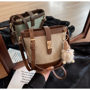 Detail of color-block canvas bucket bags with leather trim, metal turn-lock and cute charm