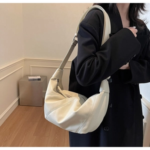 Dettaglio della borsa a mezzaluna in finta pelle crema con cuciture diagonali su modella