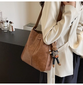 Brown vintage leather tote bag with houndstooth bunny charm detail on a minimalist cafe background