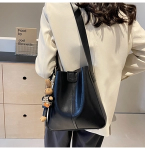 Black leather bucket bag with a cute brown plush rabbit charm shown on a model's shoulder