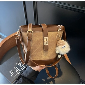 Detail of canvas bucket bag with leather trim, metal lock, and plush charm