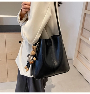 Detail of black glossy bucket bag with textured leather and a cute brown rabbit pendant