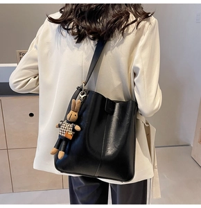 Close-up of a black minimalist tote bag with a plush bunny charm and shoulder strap detail