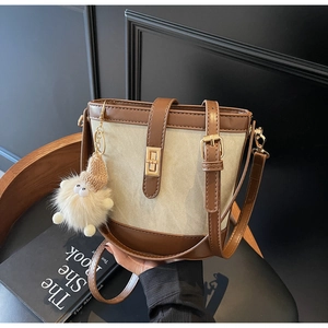 Detail of vintage canvas bucket bag with brown leather trim and plush doll charm