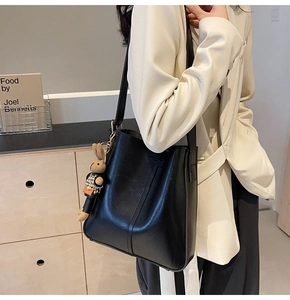 Close-up of black leather tote bag with vertical stitching and cute rabbit doll charm