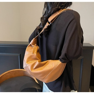 Detail of caramel brown crescent bag with soft textured leather and wide strap on model