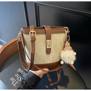 Detail of retro color-block bucket bag with canvas stitching and plush doll charm
