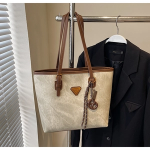 Détail d'un sac cabas gris avec texture marbrée, poignées en cuir marron et logo sur socle