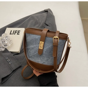Detail of blue denim bucket bag with brown leather trim and golden twist lock closure