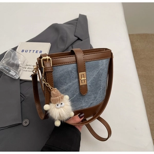 Detail of blue denim bucket bag with brown leather trim and cute white plush charm