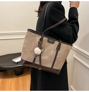 Détail d'un sac cabas gris mat avec base en cuir marron et breloque en peluche