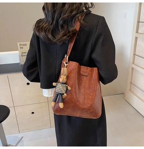 Detail of vintage brown bucket bag with plush rabbit charm and oily leather texture