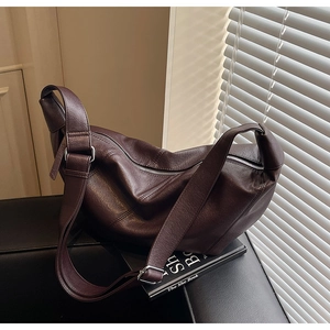 Detail of soft dark brown leather crossbody bag with silver buckle and wide shoulder strap