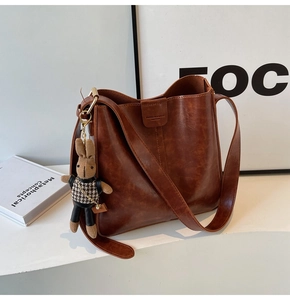 Detailed view of brown leather bucket bag with wide shoulder strap and cute rabbit charm