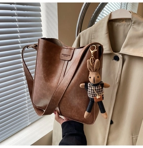 Detail of vintage brown leather bucket bag with plush rabbit charm and wide strap