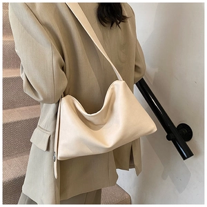Vue latérale du grand sac bandoulière beige porté par un mannequin dans un décor épuré