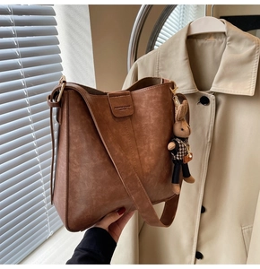 Detail view of brown vintage bucket bag with plush rabbit charm and embossed leather tag