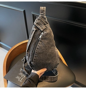 Close-up of a washed denim crossbody chest bag on a dark chair showing fabric texture