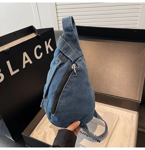 Detail view of a blue denim chest bag with black zipper inside a black luxury gift box