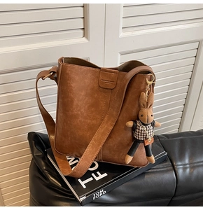 Close-up of vintage brown leather bucket bag with plush rabbit charm and wide strap