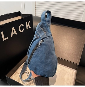 Detailed close-up of dark blue denim sling bag with silver zipper and yellow stitching