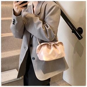 Détail du sac nuage plissé rose clair porté avec un blazer gris oversize minimaliste