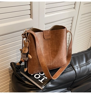 Close-up of brown leather bucket bag with brand stamp and cute rabbit doll charm detail