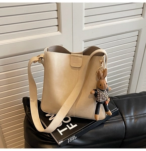 Detail of beige bucket bag with metal closure and a cute brown rabbit charm on leather sofa