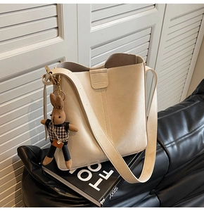 Detail of cream bucket bag with embossed lettering and a cute knitted rabbit charm
