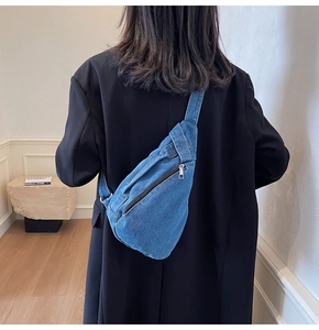 Detail view of the washed blue denim crossbody chest bag on a black blazer
