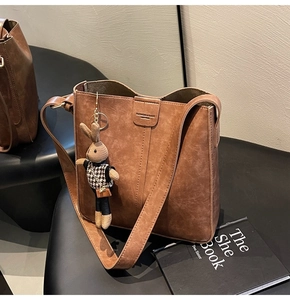 Detail of vintage brown leather bucket bag with vertical stitching and plush rabbit charm
