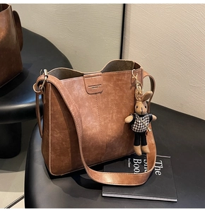 Close-up of brown leather bucket bag with fashion logo and a cute rabbit doll charm