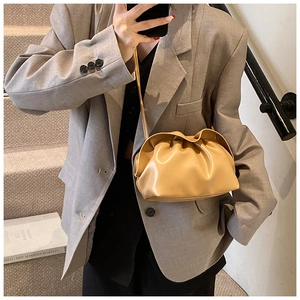 Détail du sac à main plissé marron clair porté par un mannequin sur des marches