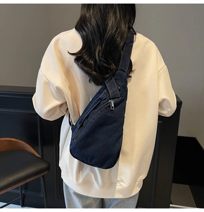 Detail view of a large navy blue denim crossbody bag worn by a model in a trendy cafe