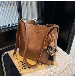 Close-up of brown PU bucket bag with vertical stitching and cute rabbit doll keychain