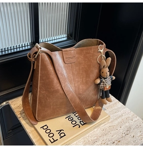 Close-up of brown vintage leather bucket bag with wide strap and rabbit charm
