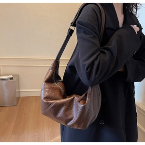 Detailed view of a brown vintage pleated leather hobo bag worn with a black blazer