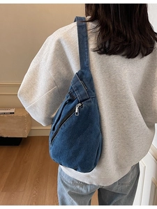 Deep blue denim crossbody sling bag with metal zipper shown on model in a minimalist room