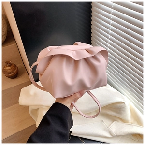 Gros plan d'un sac nuage plissé rose avec poignée fine devant un costume blanc