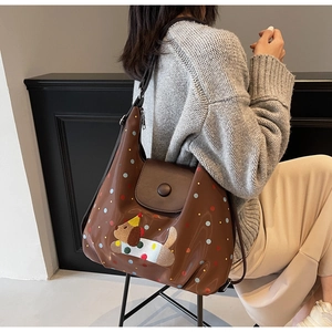 Detail of a brown leather tote bag with polka dot print and dog embroidery on a model