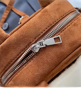 Detail of smooth silver metal zipper and brown suede texture on a small square handbag