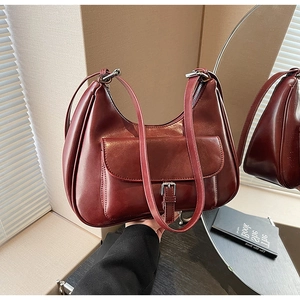 Close-up of burgundy hobo bag with glossy finish and silver buckle on a wooden desk