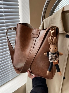 Brown leather bucket bag with wide shoulder strap and a cute knitted rabbit pendant