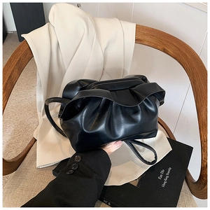 Détail du sac à main noir plissé en cuir souple posé sur une chaise en rotin vintage