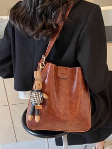 Brown retro shoulder tote bag with rabbit charm and metal buckle on faux leather texture