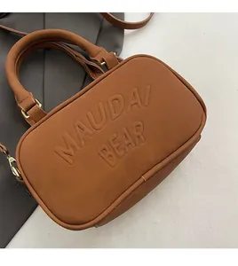 Close-up of the embossed MAUDAI BEAR lettering on a brown suede crossbody bag texture