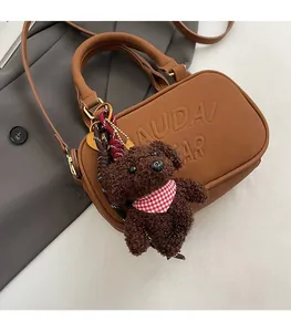 Detail of brown faux leather handbag featuring AUDAI AR embossing and a teddy bear charm