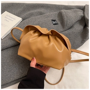 Gros plan d'un sac nuage plissé en cuir camel posé sur un manteau en tweed gris très élégant